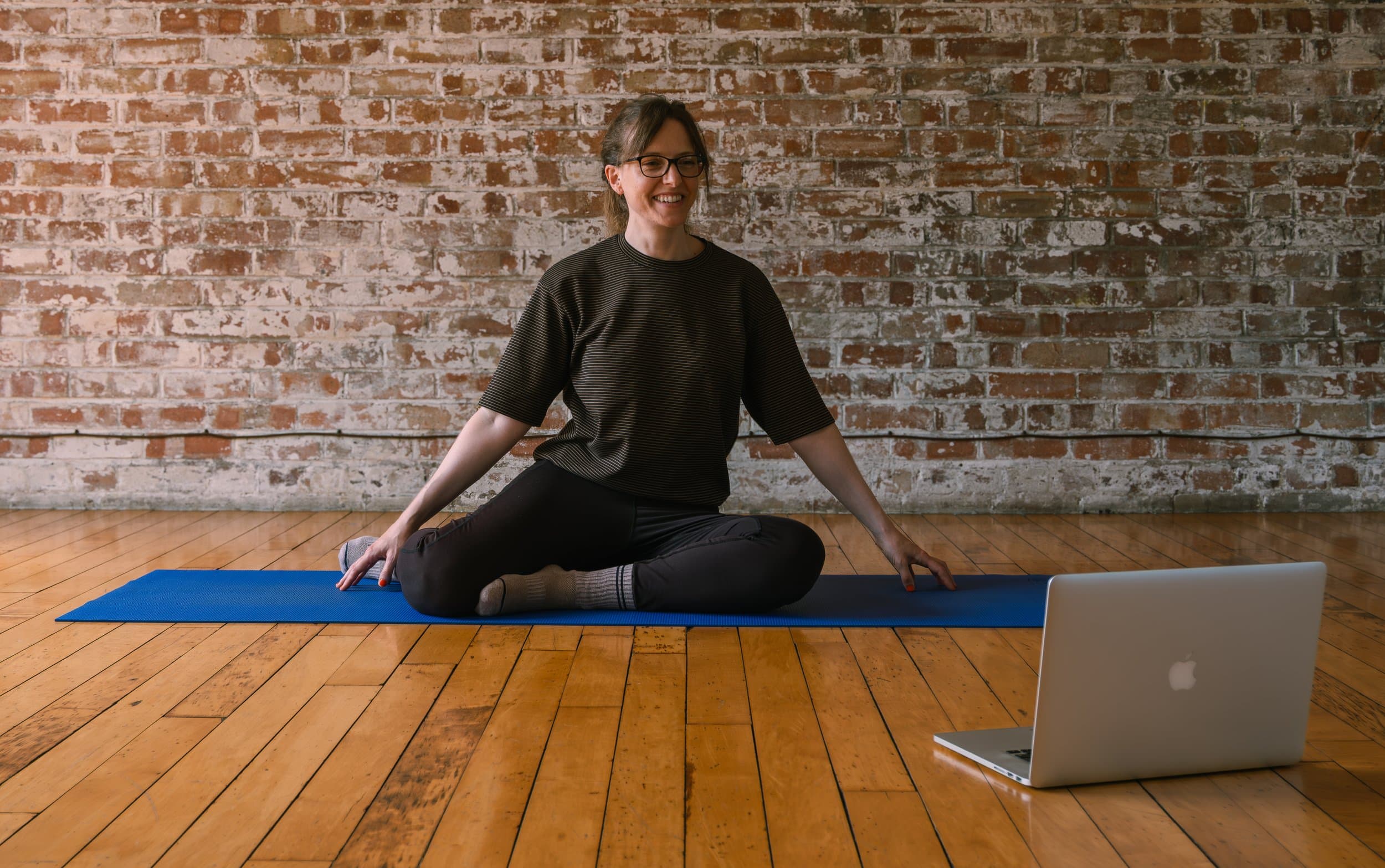 Ellen sitting on a mat in front of a laptop, set up to teach a class online